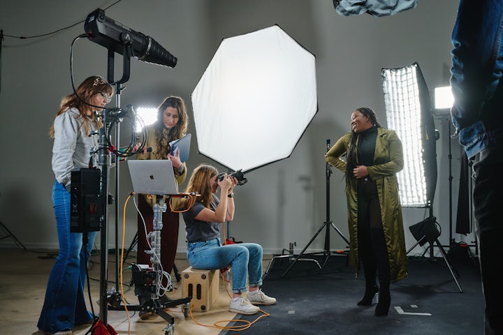 Photography studio setup with a model posing under studio lights, surrounded by a photographer and assistants adjusting equipment.